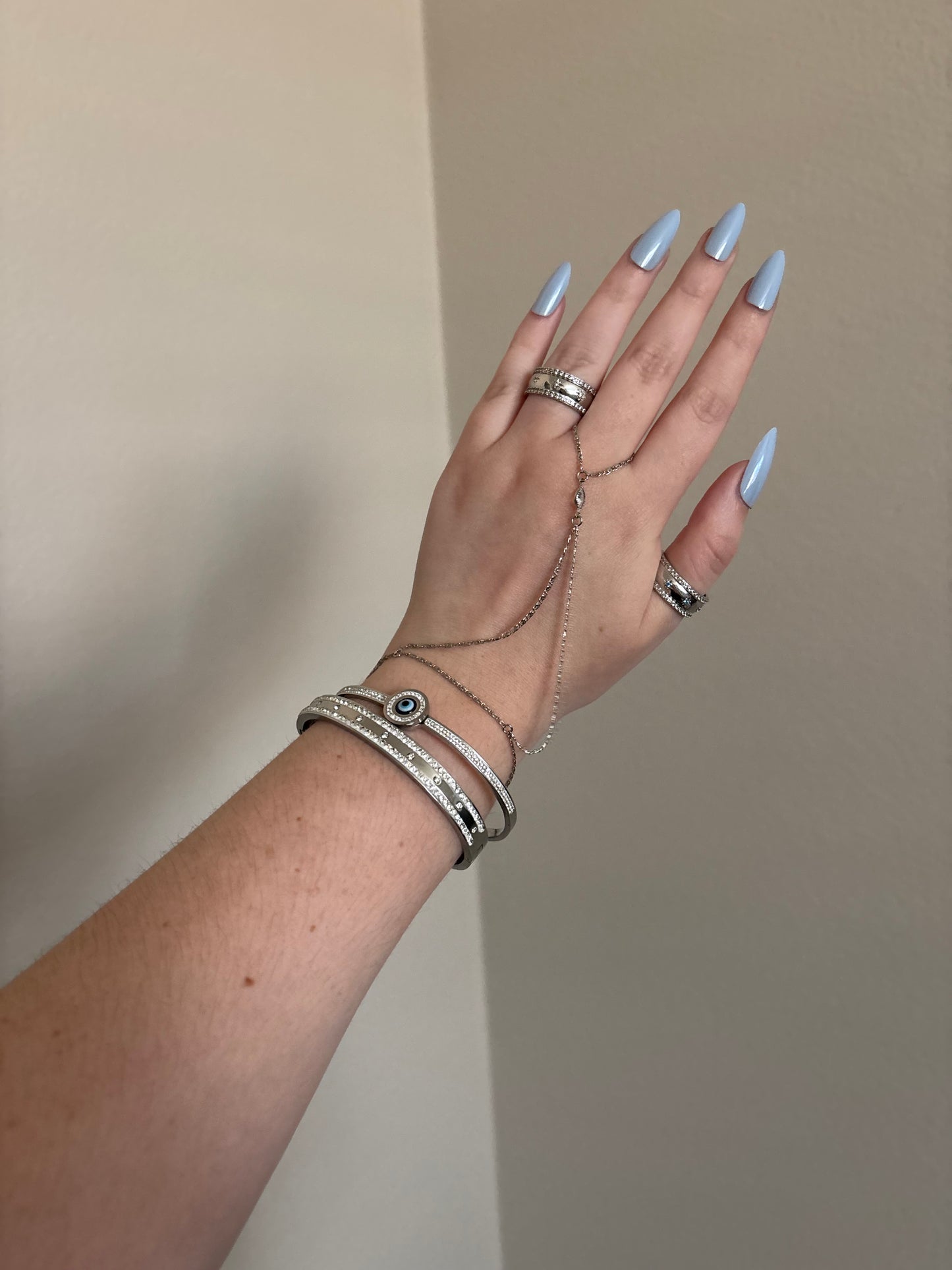 Hand with multiple silver rings and bracelets on a neutral background