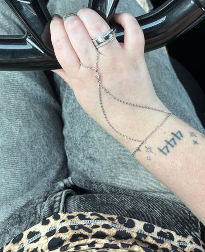 Hand with multiple rings and a bracelet, wearing gray pants with leopard print trim.