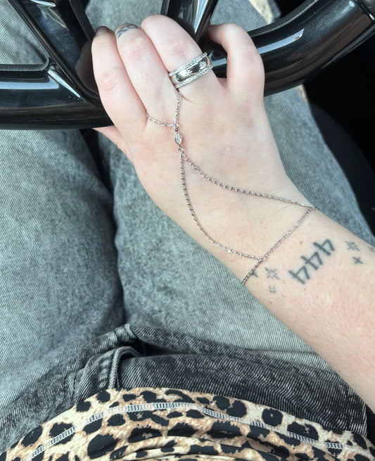 Hand with multiple rings and a bracelet, wearing gray pants with leopard print trim.