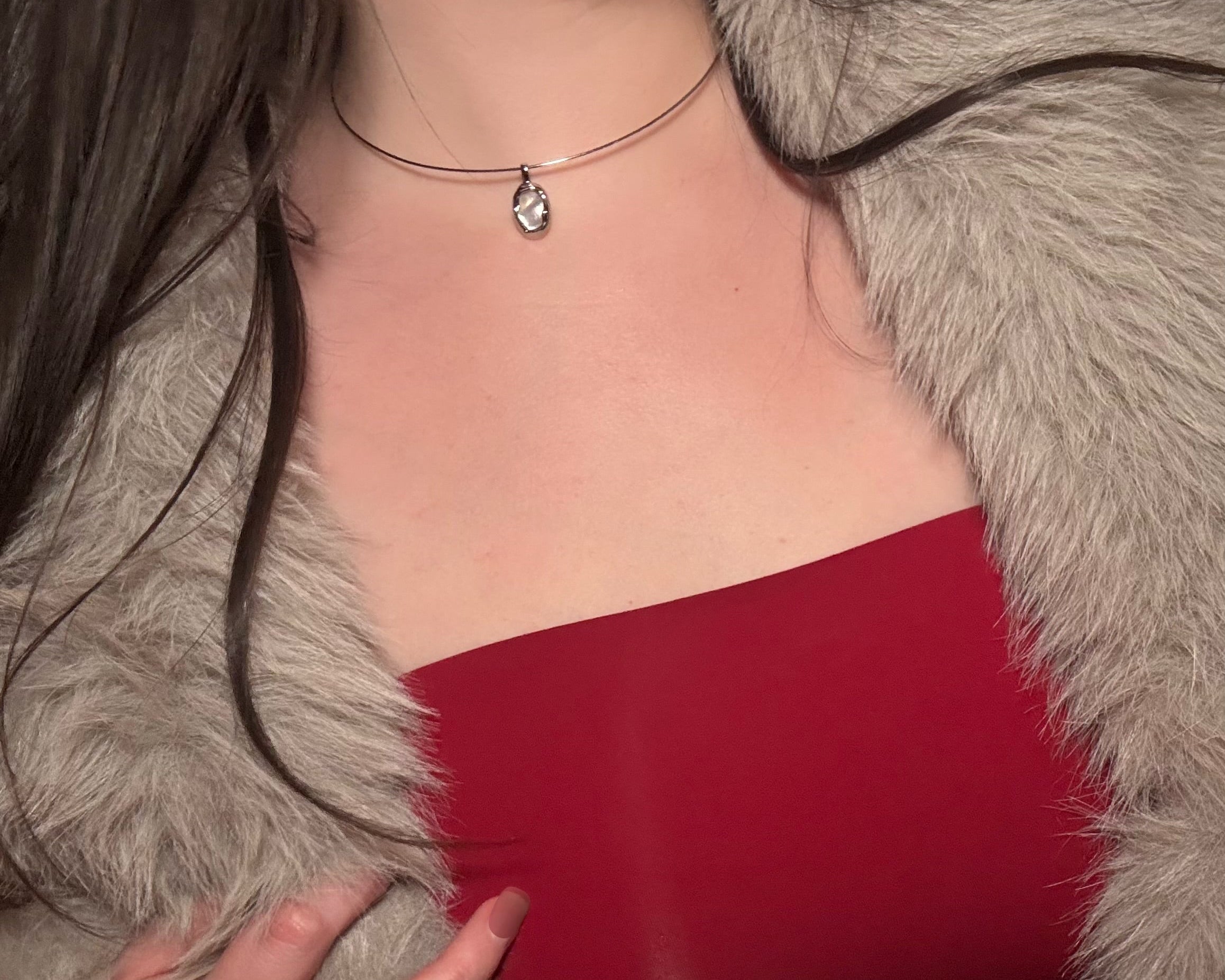 Person wearing a red top and gray fur coat with a necklace.