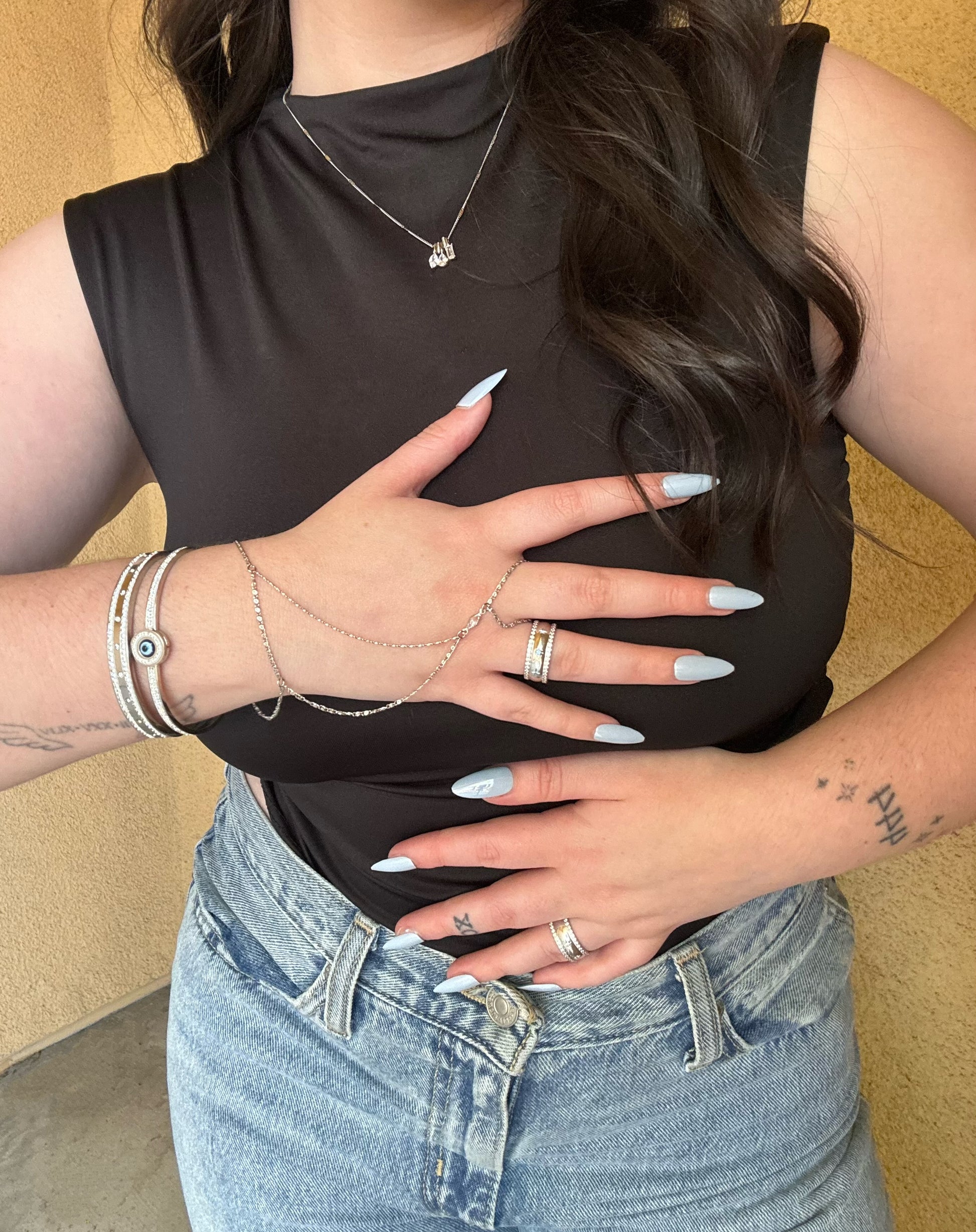 Person wearing a black sleeveless top and blue jeans with a neutral background