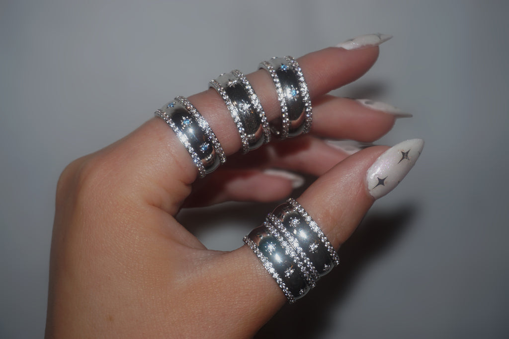 Hand wearing multiple silver rings with a neutral background